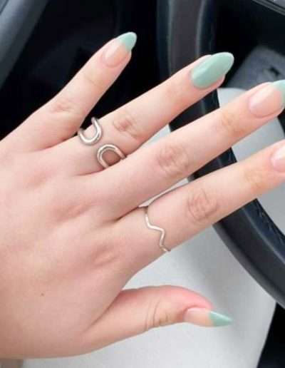 An open hand against a steering wheel with manicured teal french tips
