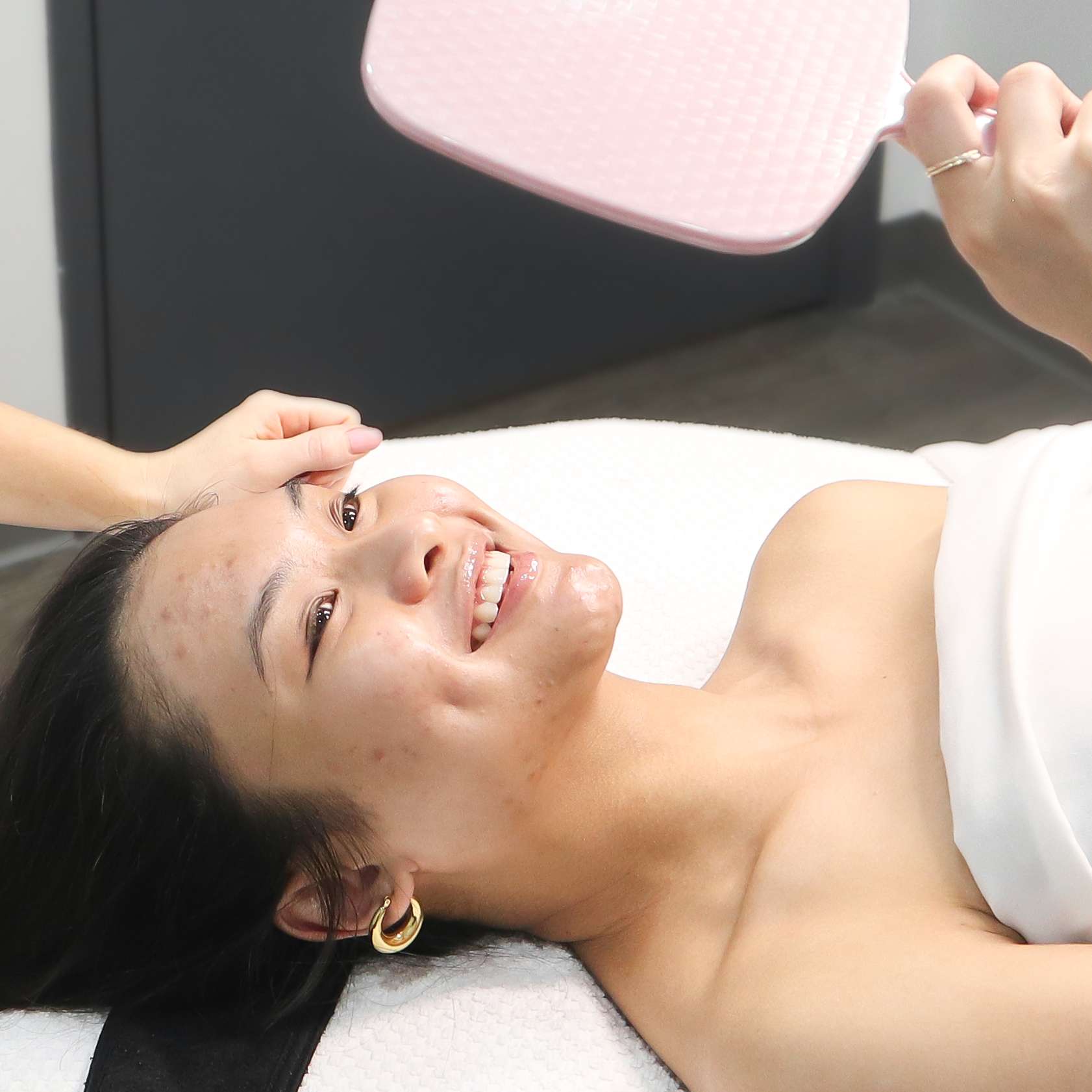 Total Wrapture Medi Spa Winnipeg Client smiling at hand held mirror after facial treatment