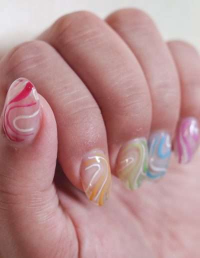 Clear manicured nails with colourful orange, green, blue, and purple, and red polish strokes.