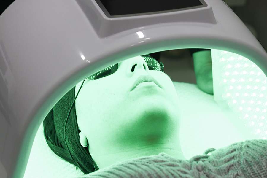 Woman's face laying beneath green LED light therapy machine.