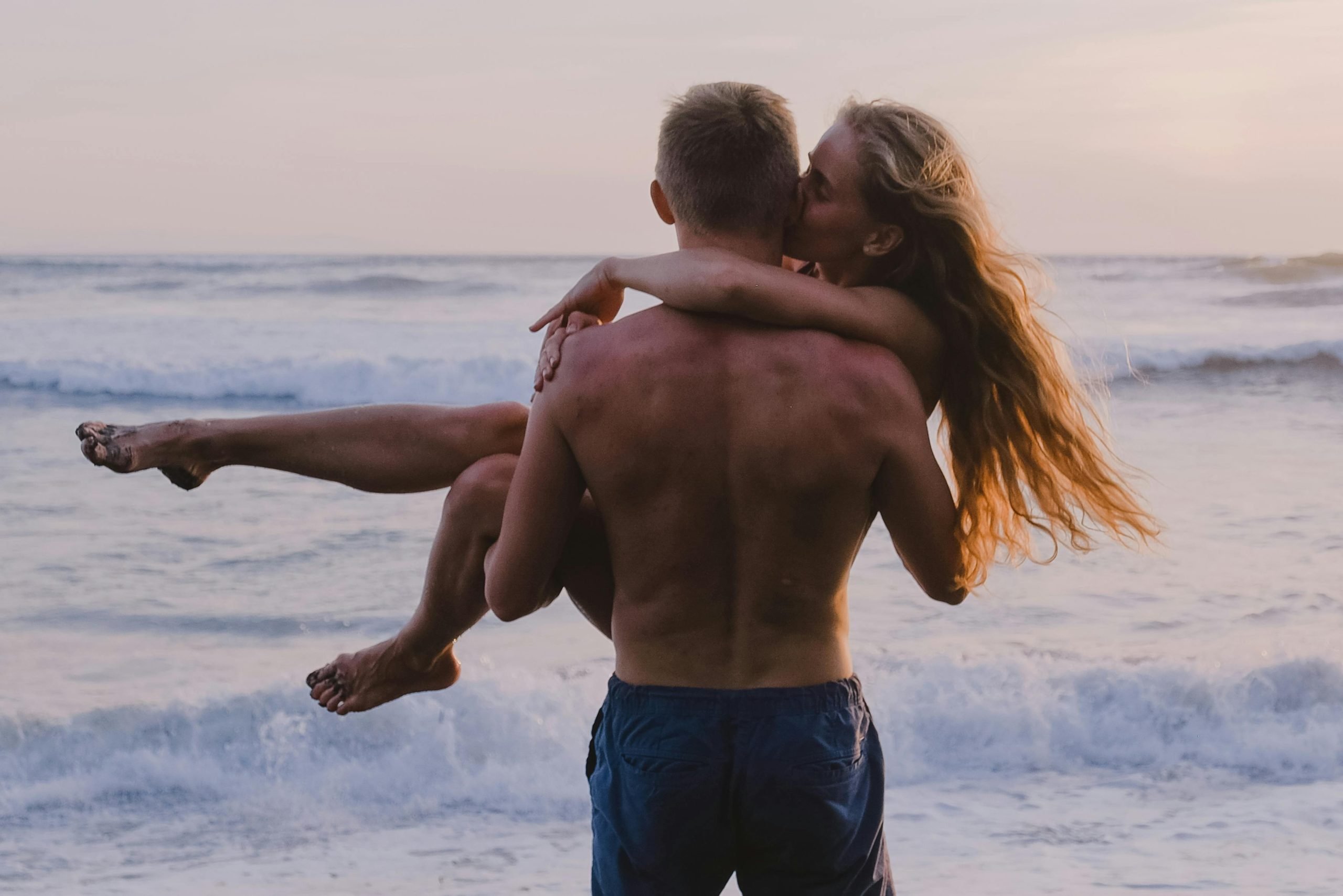 A man with a hair free back carrying a romantic partner on the beach