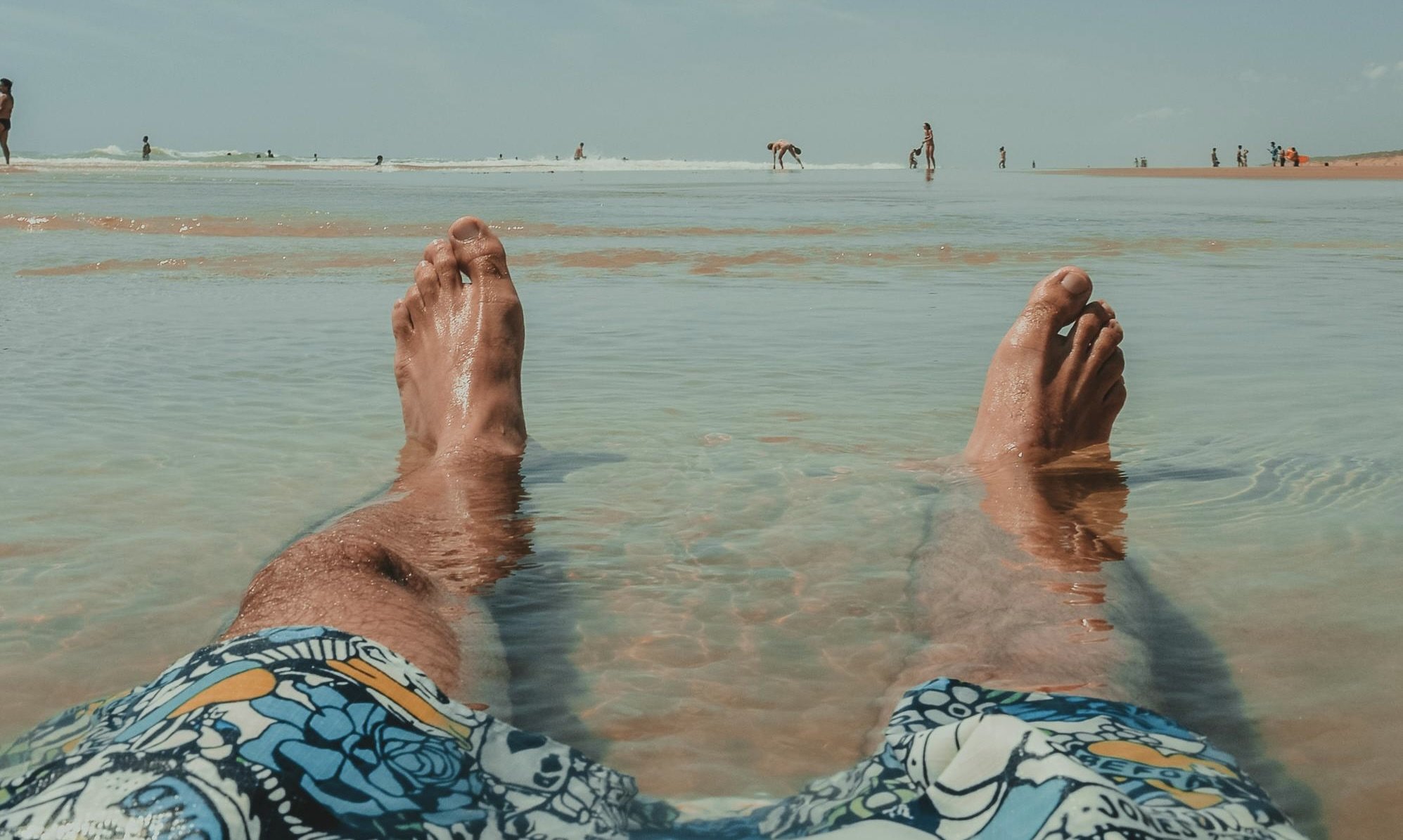 a pair of legs with feet sticking out of the water in a beach setting. the person has gotten a male pedicure in winnipeg